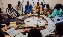 African teenage boys dressed in robes sit in a circle on the floor of a room with books in Arabic script open in front of them