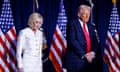 a woman and a man stand with their heads bowed in front of American flags