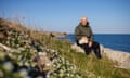 Author and naturalist Andrew Cleave sat on a group of rocks at Portland Bill, Dorset, UK on a blue-sky day.