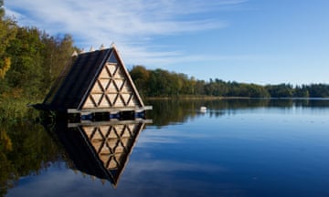 A triangular wooden sauna floating on a lake