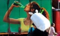A man carries a sack on his shoulder in front of signage of a woman drinking from a green bottle