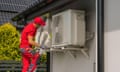 A worker inspects an air conditioning unit outside a building