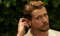 Jack O’Connell in a white polo shirt, touching his right ear