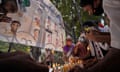 people light candles at a memorial showing photos of deceased people