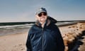 A man in a cap and sunglasses stands on a beach