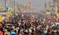 A huge number of South Asians are seen walking along between shacks, vehicles and temporary lighting and electricity poles