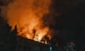 Flames reflected in smoke above a silhouetted building and trees