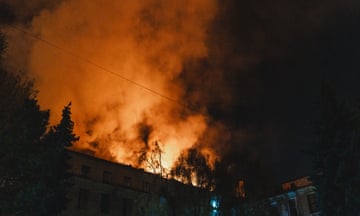 Flames reflected in smoke above a silhouetted building and trees