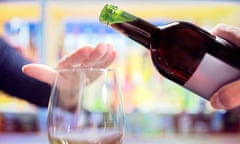 A hand covers a wine glass refusing a top-up from a pouring bottle.