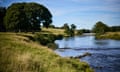 The River Derwent on a sunny day with grassy slopes and trees in full leaf either side of it