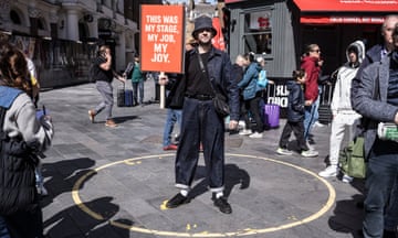 Street performer standing in a crowd with a placard